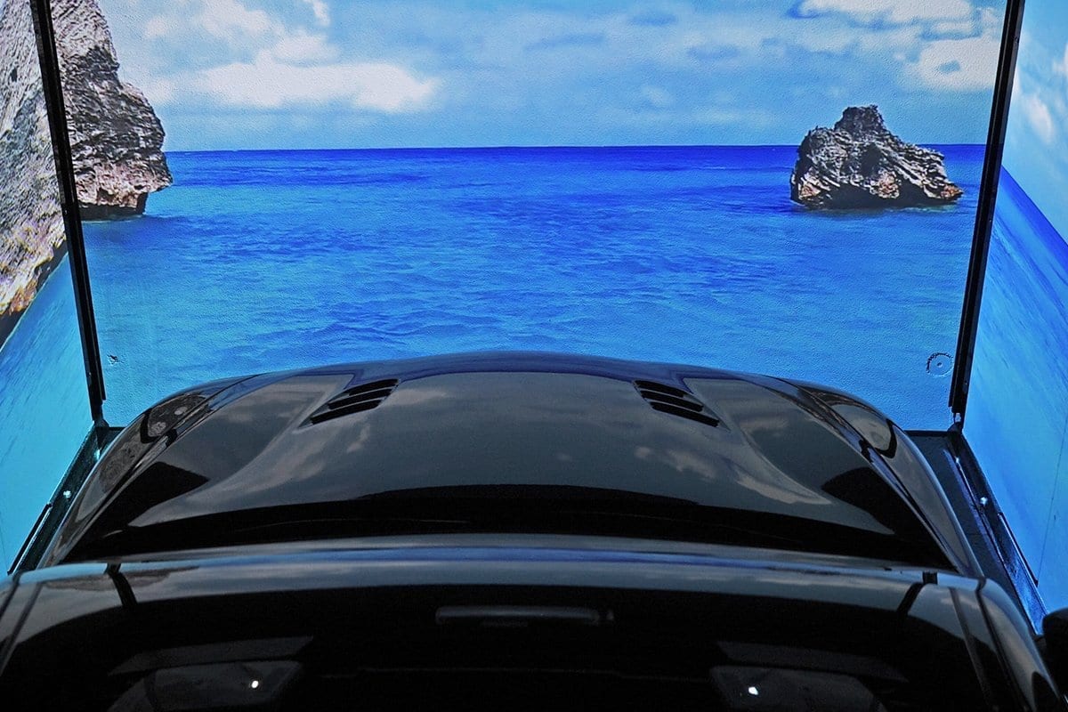 Voiture noire vue de l'intérieur avec toit panoramique ouvert, vue sur la mer bleue avec rochers et ciel bleu