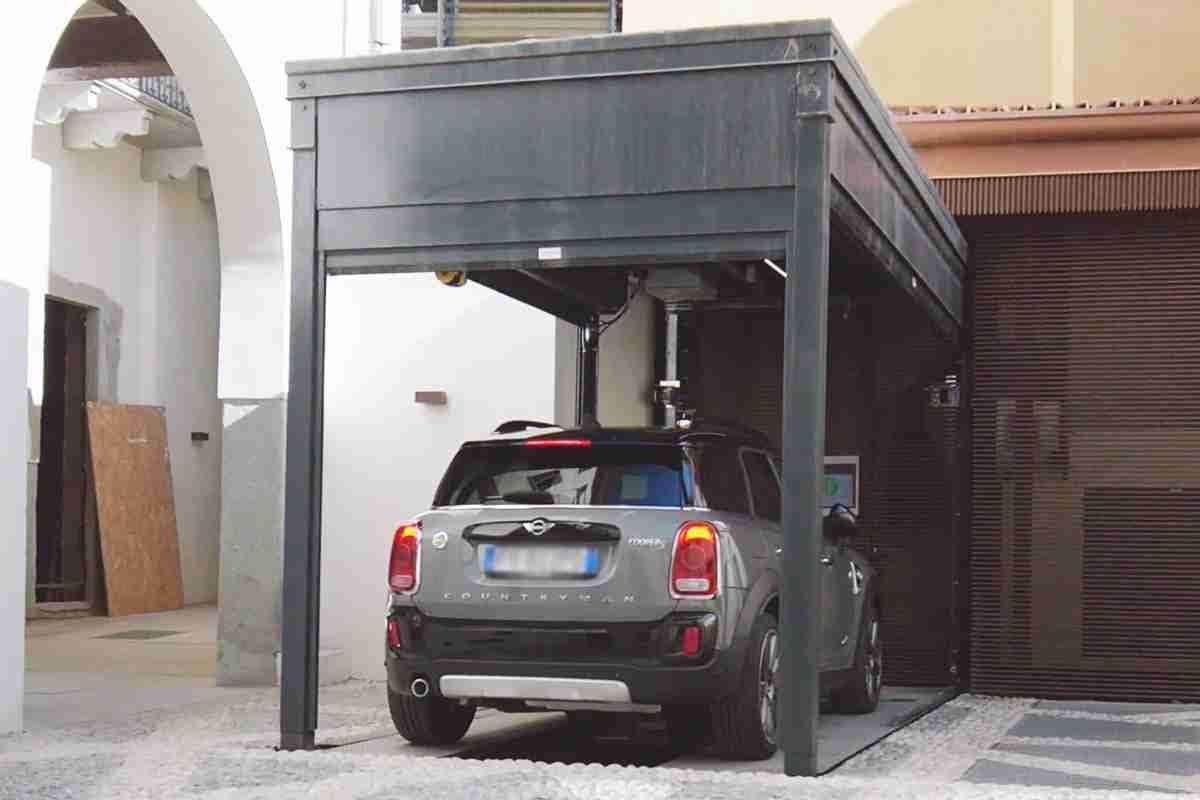 Voiture grise garée sous structure métallique grise avec toit, cour intérieure avec bâtiments résidentiels