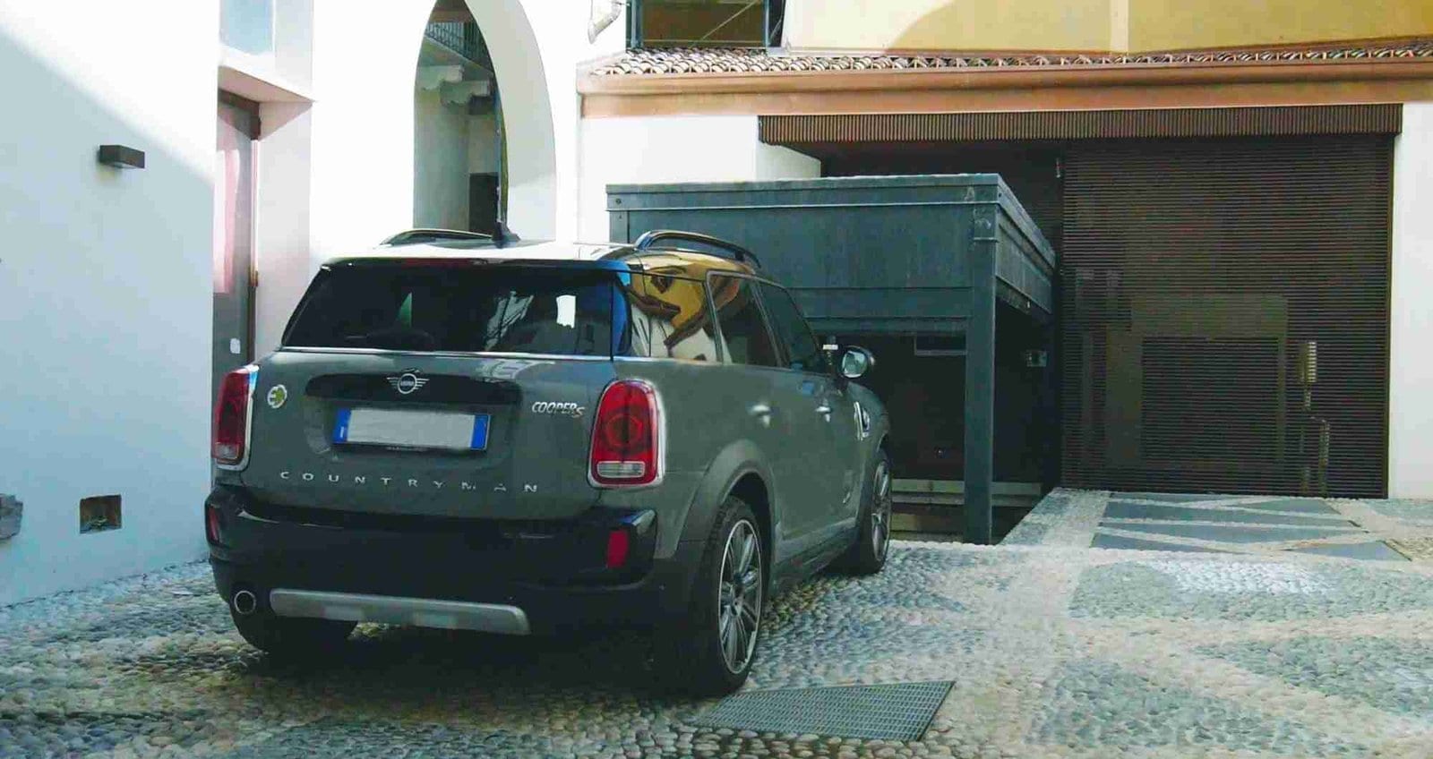 Voiture verte garée devant structure métallique verte, cour avec bâtiments résidentiels en arrière-plan